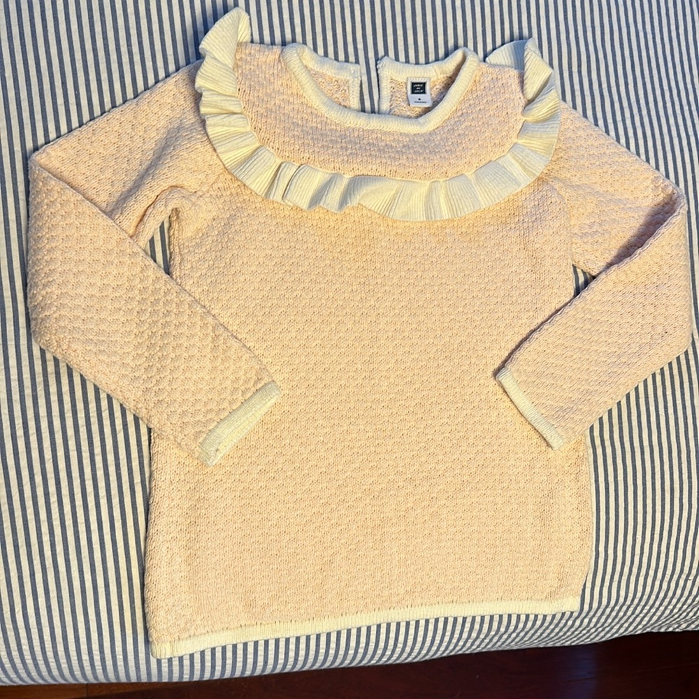 Girls light pink sweater with white trim and white ruffles along the top.